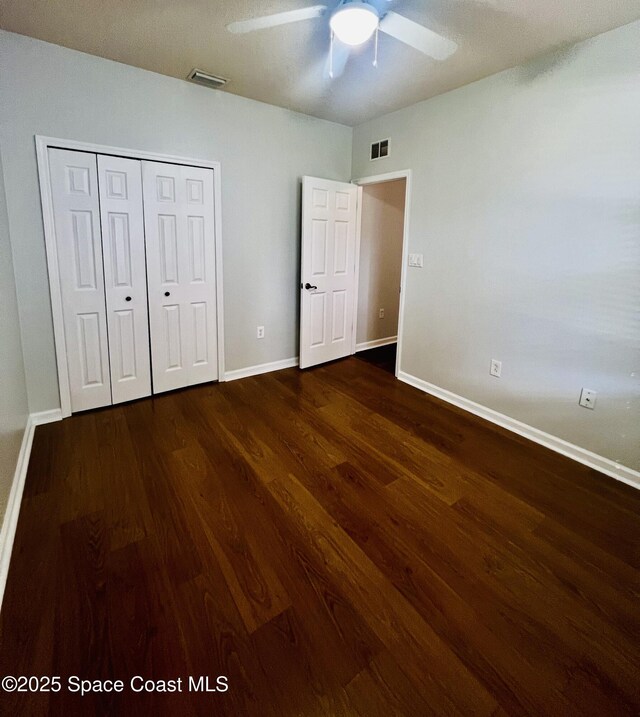 unfurnished bedroom featuring dark wood-type flooring, baseboards, visible vents, and a closet