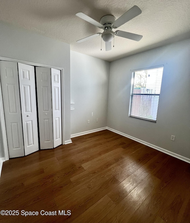 unfurnished bedroom featuring a closet, a textured ceiling, baseboards, and dark wood-style flooring