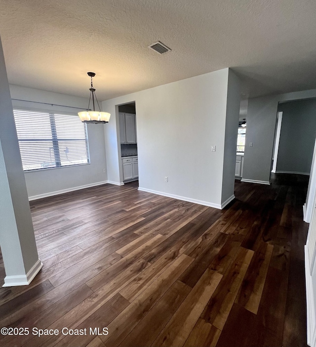 unfurnished dining area featuring visible vents, a textured ceiling, baseboards, and dark wood-style flooring