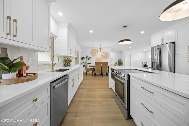 kitchen featuring sink, white cabinetry, pendant lighting, stainless steel appliances, and light hardwood / wood-style floors