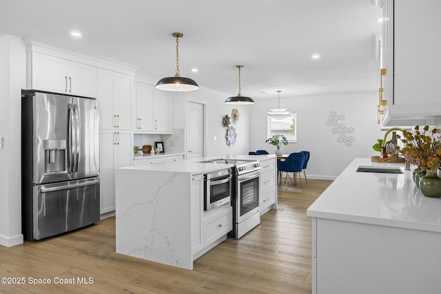 kitchen featuring stainless steel appliances, pendant lighting, a center island with sink, and white cabinets