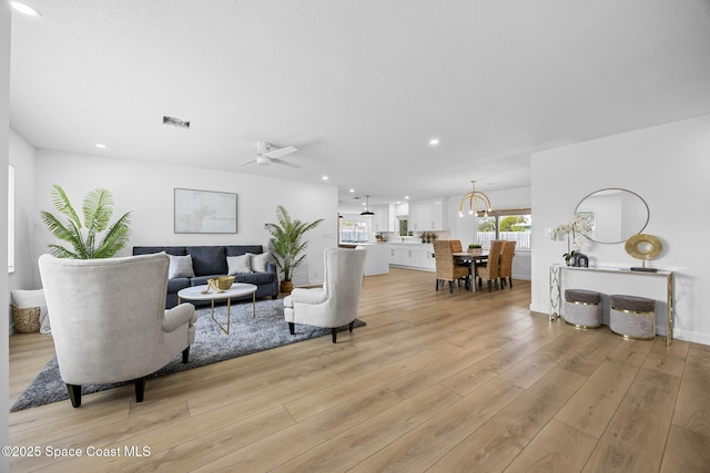 living room with ceiling fan with notable chandelier, a textured ceiling, and light wood-type flooring