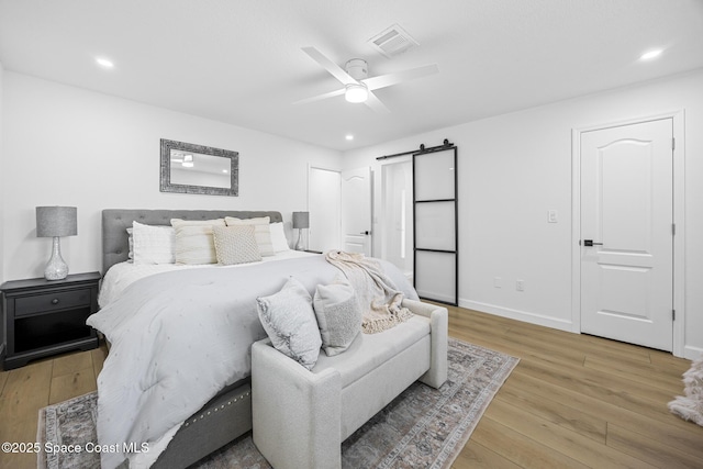 bedroom featuring light hardwood / wood-style floors, a barn door, and ceiling fan