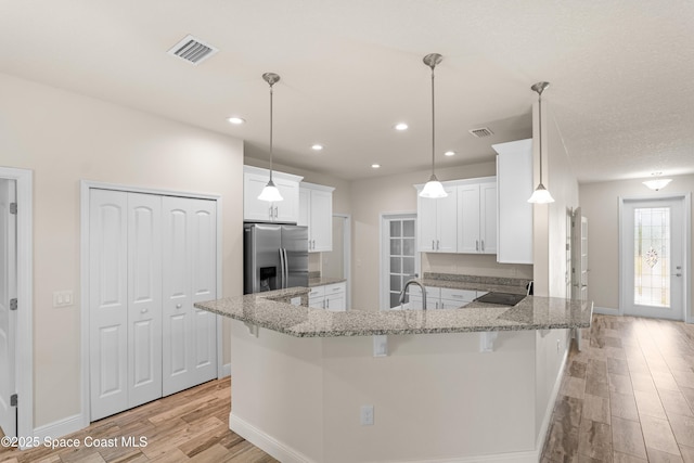 kitchen with stainless steel fridge with ice dispenser, a kitchen breakfast bar, kitchen peninsula, and white cabinets