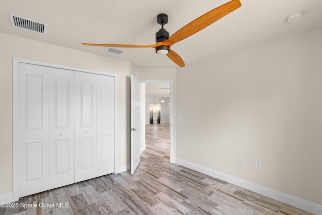 unfurnished bedroom featuring ceiling fan, a textured ceiling, a closet, and light wood-type flooring