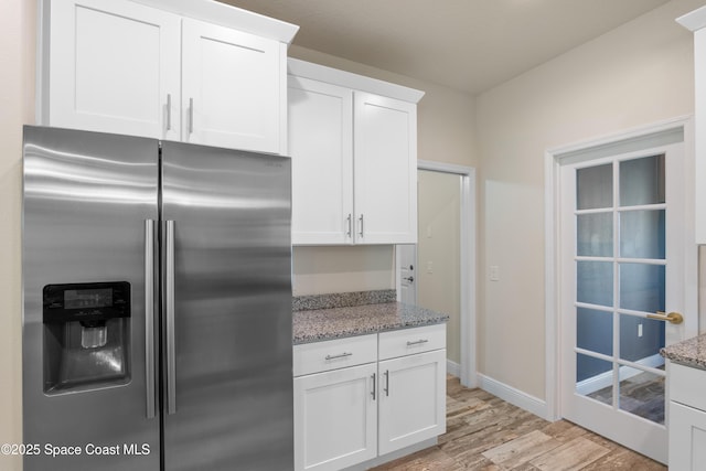 kitchen with stainless steel refrigerator with ice dispenser, white cabinetry, light stone countertops, and light hardwood / wood-style floors