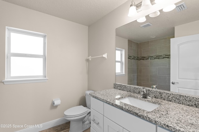 bathroom featuring a tile shower, hardwood / wood-style flooring, vanity, toilet, and a textured ceiling