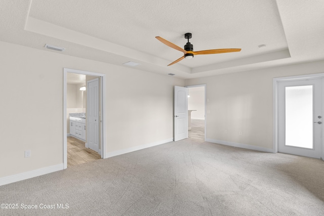 unfurnished bedroom with a raised ceiling, connected bathroom, light colored carpet, and a textured ceiling