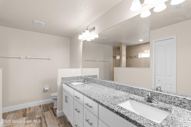 bathroom with a tile shower, hardwood / wood-style flooring, vanity, toilet, and a textured ceiling