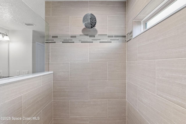 bathroom with a textured ceiling and a tile shower