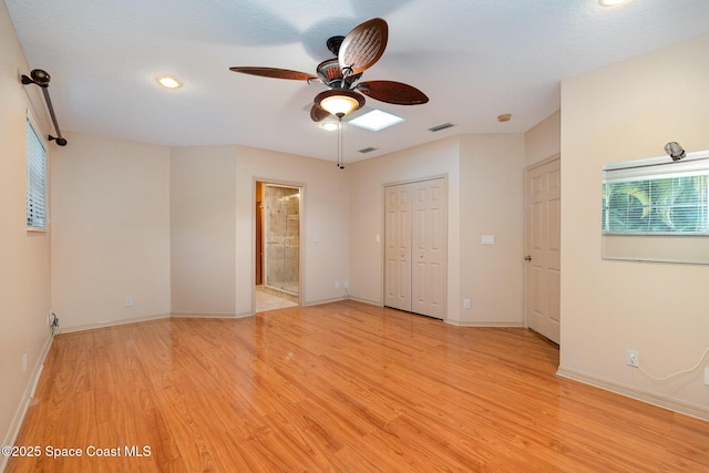 unfurnished bedroom featuring ceiling fan, ensuite bath, a closet, and light wood-type flooring