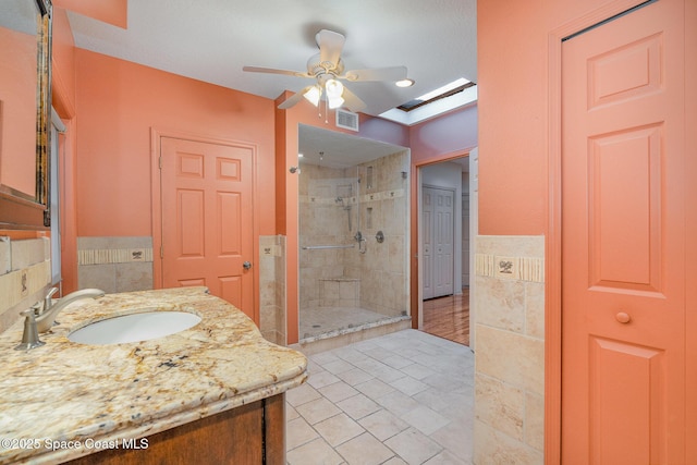 bathroom featuring a skylight, a shower with shower door, tile walls, vanity, and ceiling fan