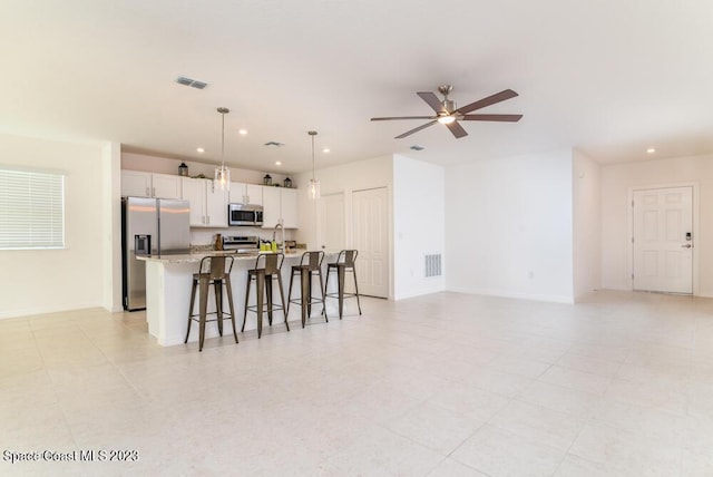 kitchen featuring white cabinetry, light stone counters, hanging light fixtures, appliances with stainless steel finishes, and a kitchen island with sink