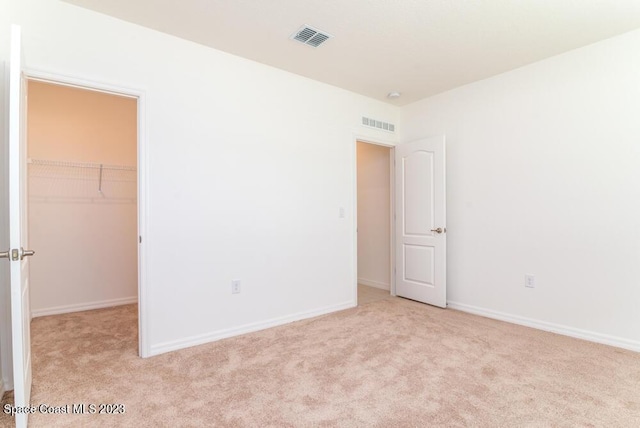 unfurnished bedroom featuring a walk in closet, light colored carpet, and a closet