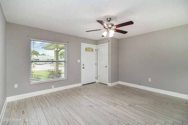 empty room featuring light wood finished floors, a textured ceiling, a ceiling fan, and baseboards