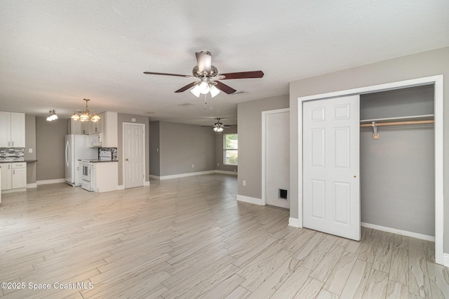 unfurnished living room with a textured ceiling, ceiling fan with notable chandelier, light wood-type flooring, and baseboards