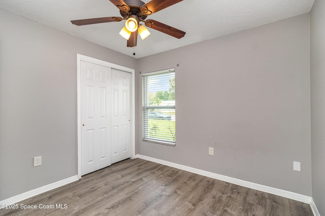 unfurnished bedroom with baseboards, wood finished floors, a closet, a textured ceiling, and a ceiling fan