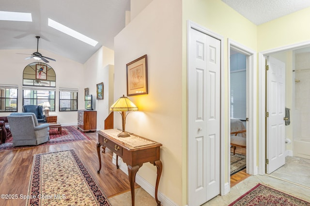 hallway featuring lofted ceiling with skylight, a textured ceiling, and light hardwood / wood-style floors