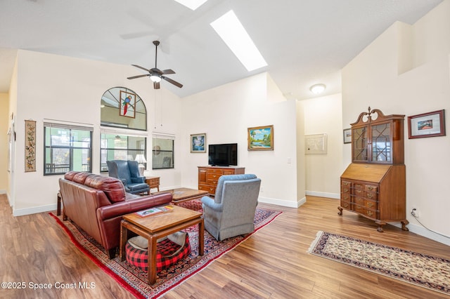 living room with a skylight, high vaulted ceiling, ceiling fan, and light wood-type flooring