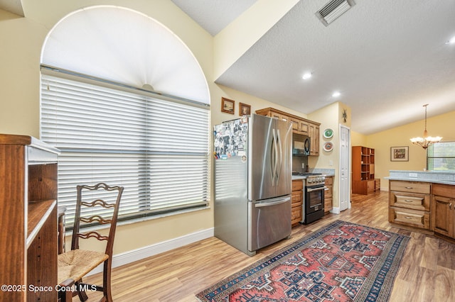 kitchen with lofted ceiling, stainless steel appliances, decorative light fixtures, and light hardwood / wood-style flooring