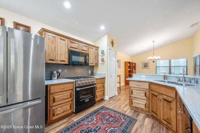 kitchen with appliances with stainless steel finishes, pendant lighting, lofted ceiling, sink, and decorative backsplash