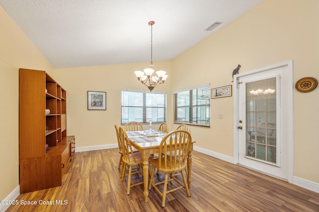 dining space with vaulted ceiling, wood-type flooring, a textured ceiling, and an inviting chandelier