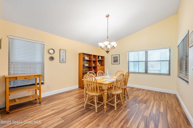 dining area with wood-type flooring, a chandelier, vaulted ceiling, and a textured ceiling