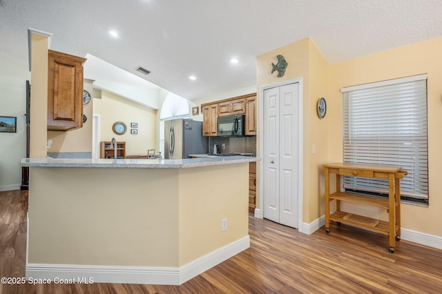 kitchen with lofted ceiling, a textured ceiling, stainless steel fridge, kitchen peninsula, and hardwood / wood-style floors