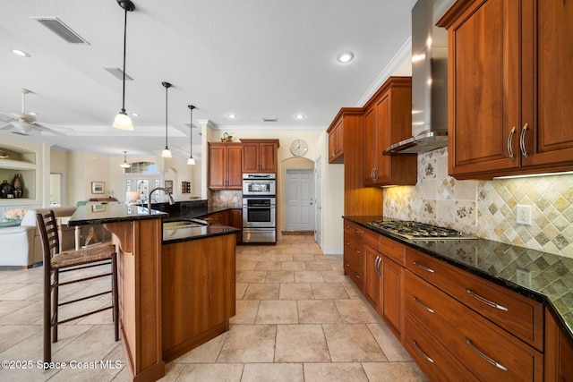 kitchen with appliances with stainless steel finishes, decorative light fixtures, sink, a kitchen breakfast bar, and wall chimney exhaust hood