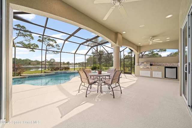 view of swimming pool featuring a patio, a water view, ceiling fan, and an outdoor kitchen