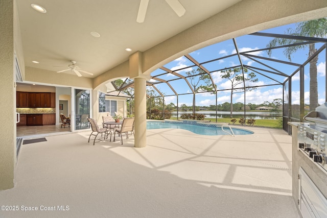 view of swimming pool featuring ceiling fan, a patio, a water view, glass enclosure, and an outdoor kitchen