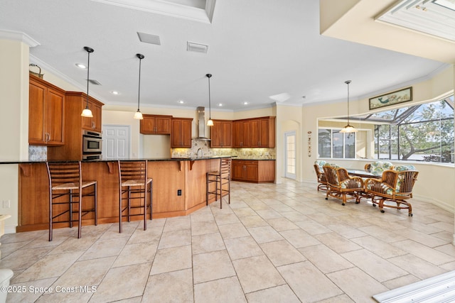 kitchen featuring wall chimney exhaust hood, ornamental molding, a kitchen breakfast bar, stone counters, and backsplash