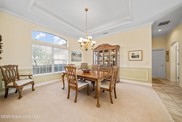 dining area with a chandelier, light colored carpet, ornamental molding, and a raised ceiling