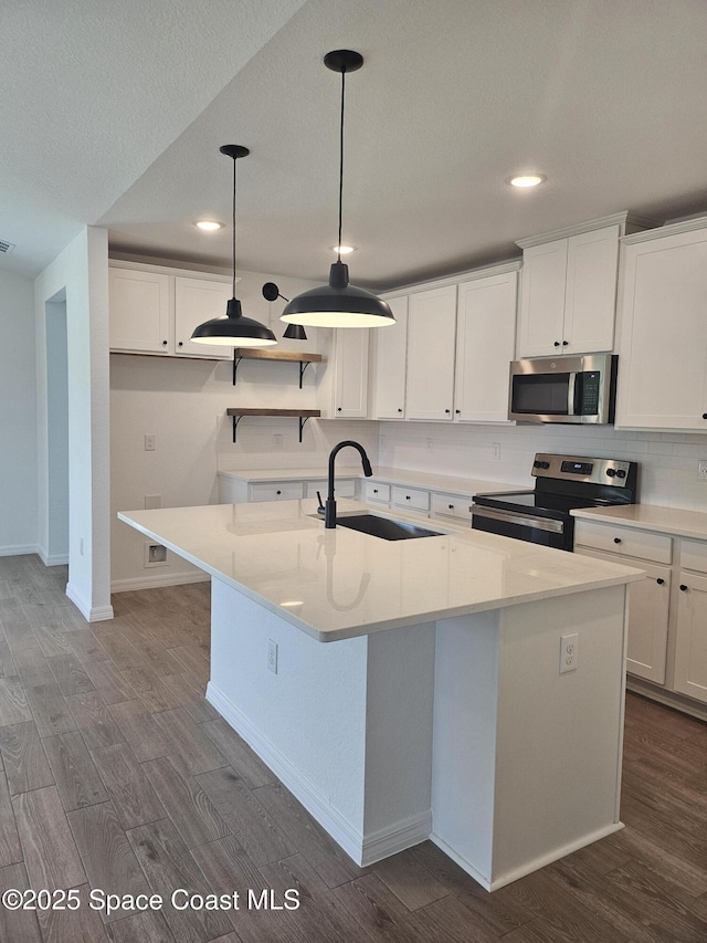 kitchen featuring sink, appliances with stainless steel finishes, a kitchen island with sink, hanging light fixtures, and white cabinetry