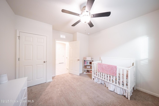 carpeted bedroom featuring ceiling fan and a crib