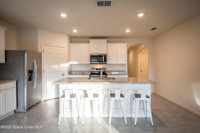 kitchen with sink, light stone counters, stainless steel appliances, a kitchen island with sink, and white cabinets