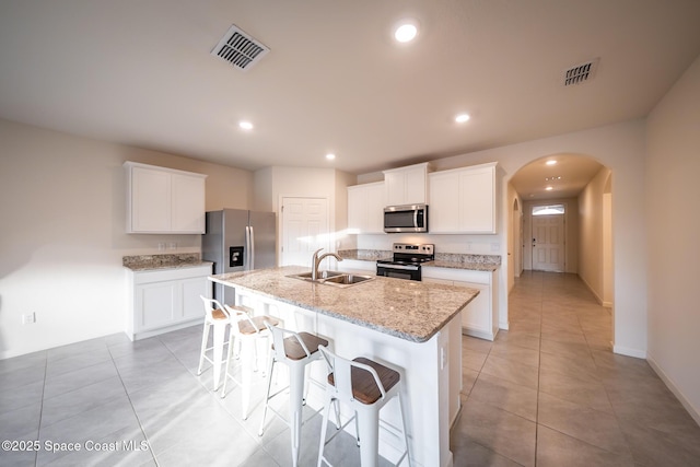 kitchen with an island with sink, appliances with stainless steel finishes, white cabinets, and light stone counters