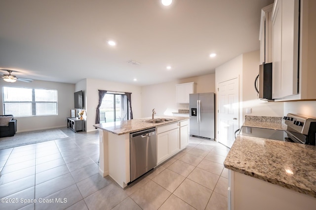 kitchen with sink, a kitchen island with sink, stainless steel appliances, light stone countertops, and white cabinets