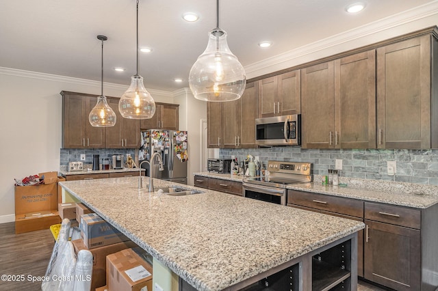 kitchen with appliances with stainless steel finishes, decorative light fixtures, an island with sink, sink, and light stone counters