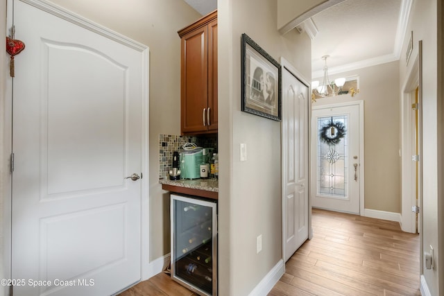 bar with backsplash, a notable chandelier, ornamental molding, light hardwood / wood-style floors, and beverage cooler