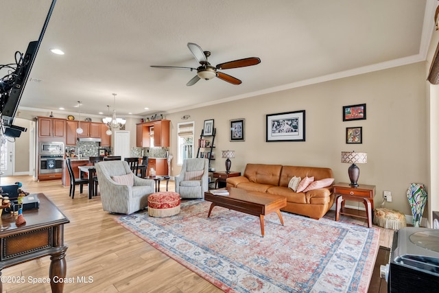 living room featuring ceiling fan with notable chandelier, ornamental molding, and light hardwood / wood-style floors