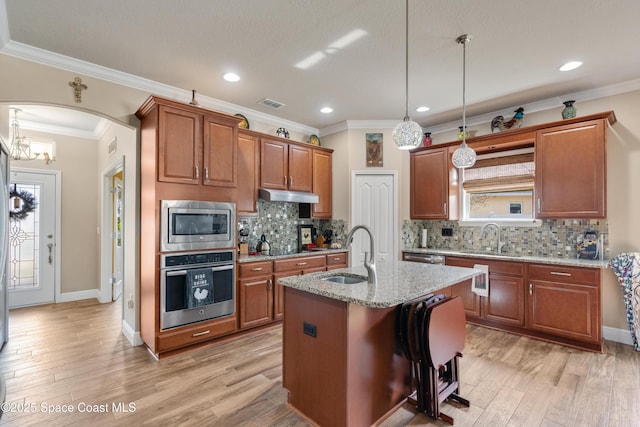 kitchen featuring an island with sink, sink, hanging light fixtures, light stone counters, and stainless steel appliances