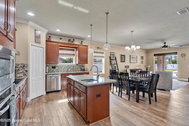 kitchen featuring an island with sink, sink, hanging light fixtures, light stone counters, and stainless steel appliances