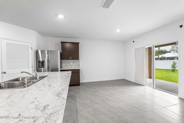 kitchen featuring sink, backsplash, dark brown cabinets, a textured ceiling, and stainless steel fridge with ice dispenser