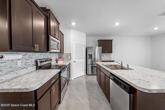 kitchen featuring a kitchen island with sink, a sink, appliances with stainless steel finishes, light countertops, and dark brown cabinets