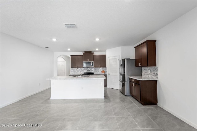 kitchen featuring visible vents, a kitchen island with sink, a sink, dark brown cabinets, and appliances with stainless steel finishes