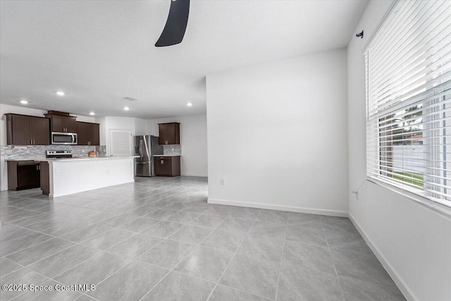 unfurnished living room with light tile patterned floors, a ceiling fan, and baseboards