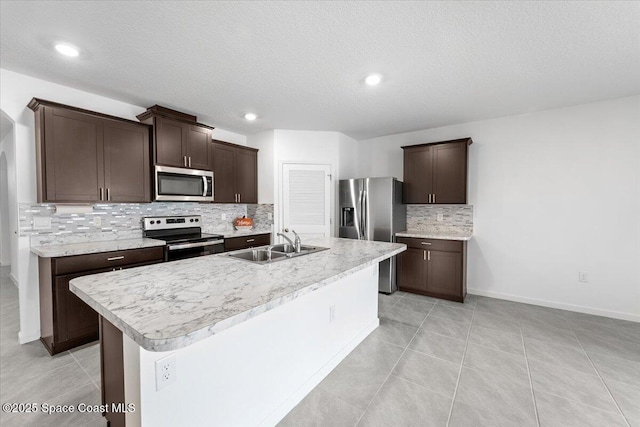 kitchen with a center island with sink, a sink, light countertops, dark brown cabinetry, and appliances with stainless steel finishes