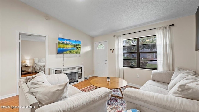 living room featuring vaulted ceiling, a textured ceiling, and light hardwood / wood-style floors