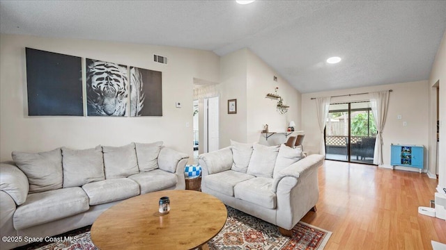 living room featuring lofted ceiling, light hardwood / wood-style flooring, and a textured ceiling